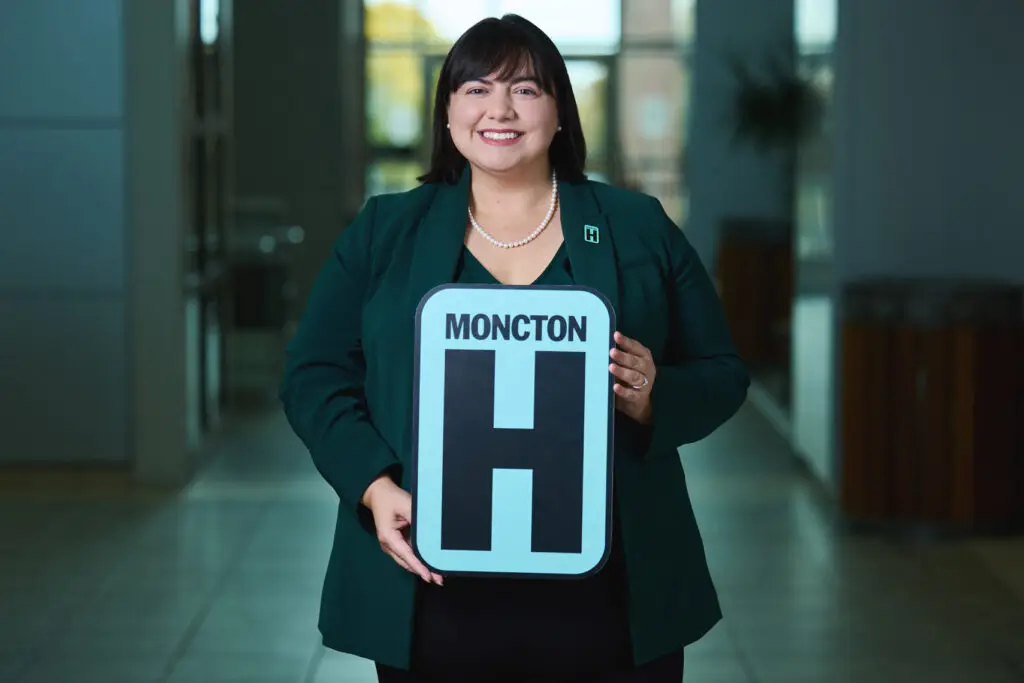 Frances LeBlanc Holding H Sign and Smiling at camera